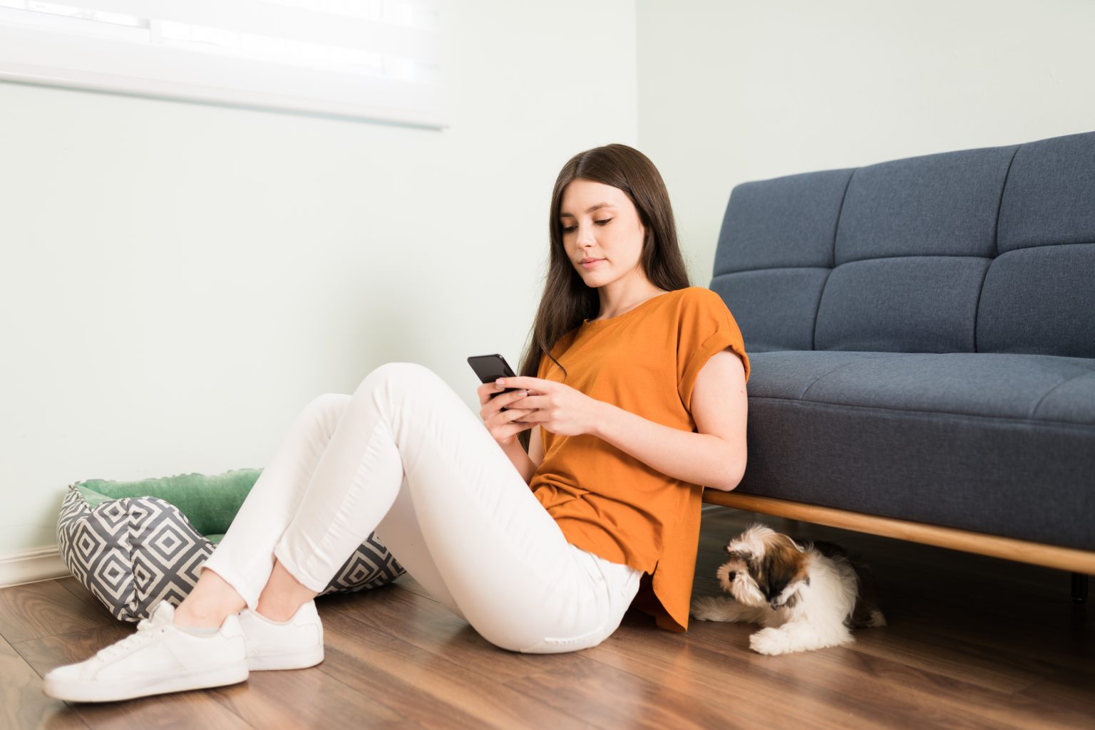 Une jeune femme séduisante se détend à la maison et envoie des SMS sur son smartphone pendant que son chien attend patiemment de jouer